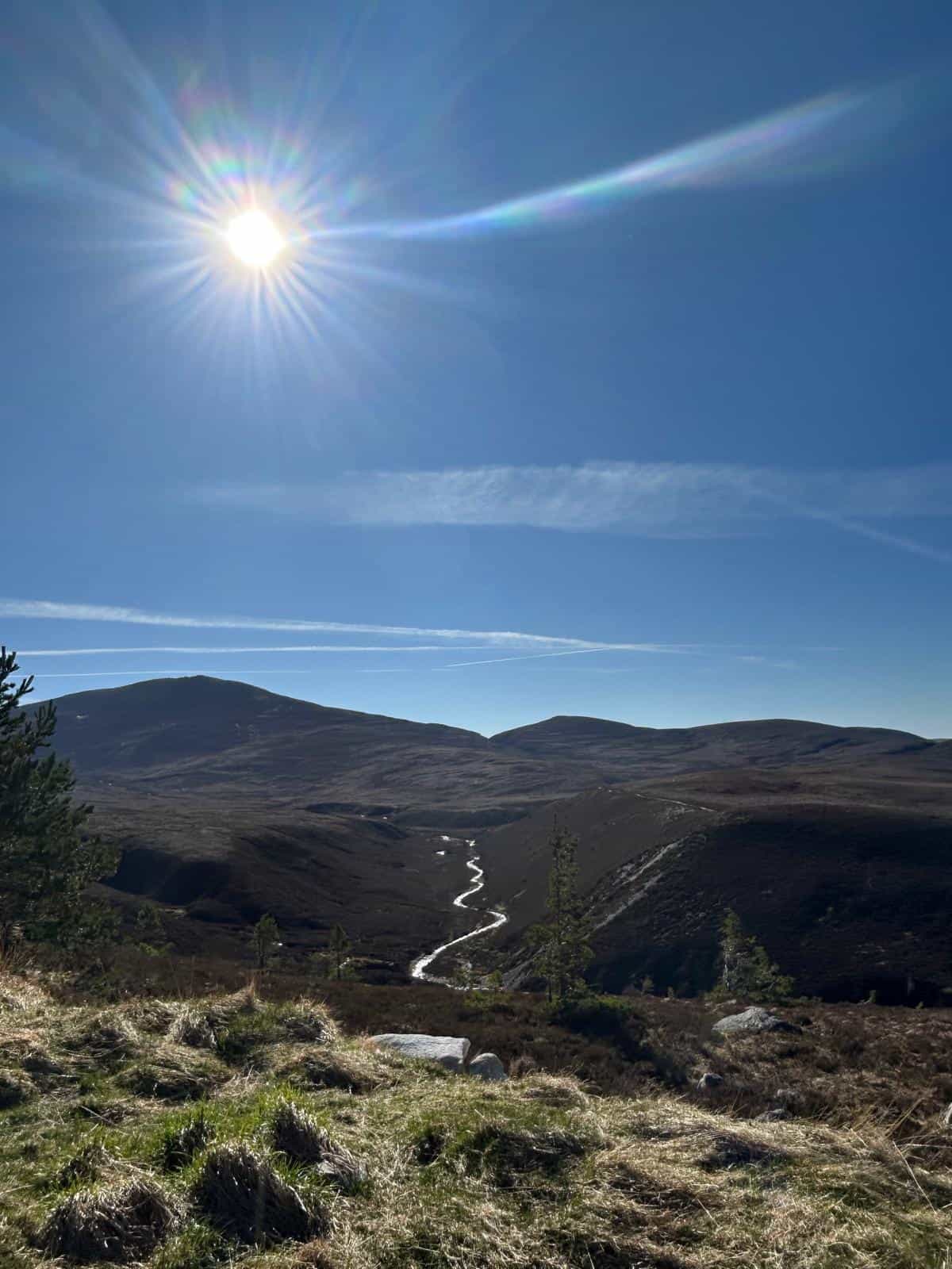 The sun shines brightly over a valley and a stream.